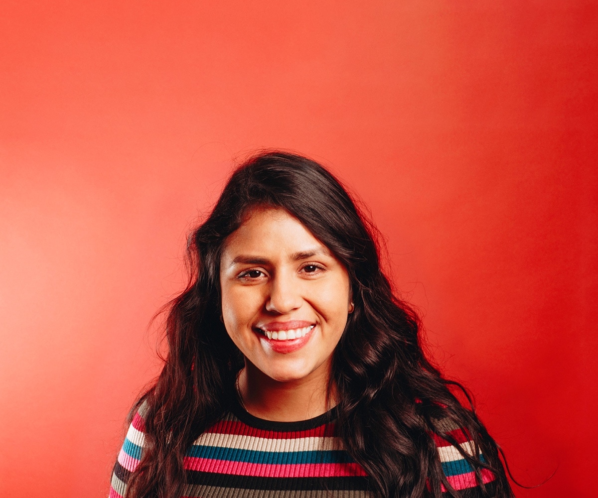 Liliana Espinoza, a leader who uses NationBuilder, in a striped shirt smiling on a red background