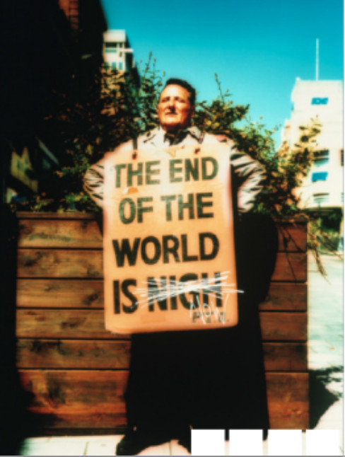 photo of man wearing a sign 'THE END OF THE WORLD IS NIGH (crossed out) NOW'