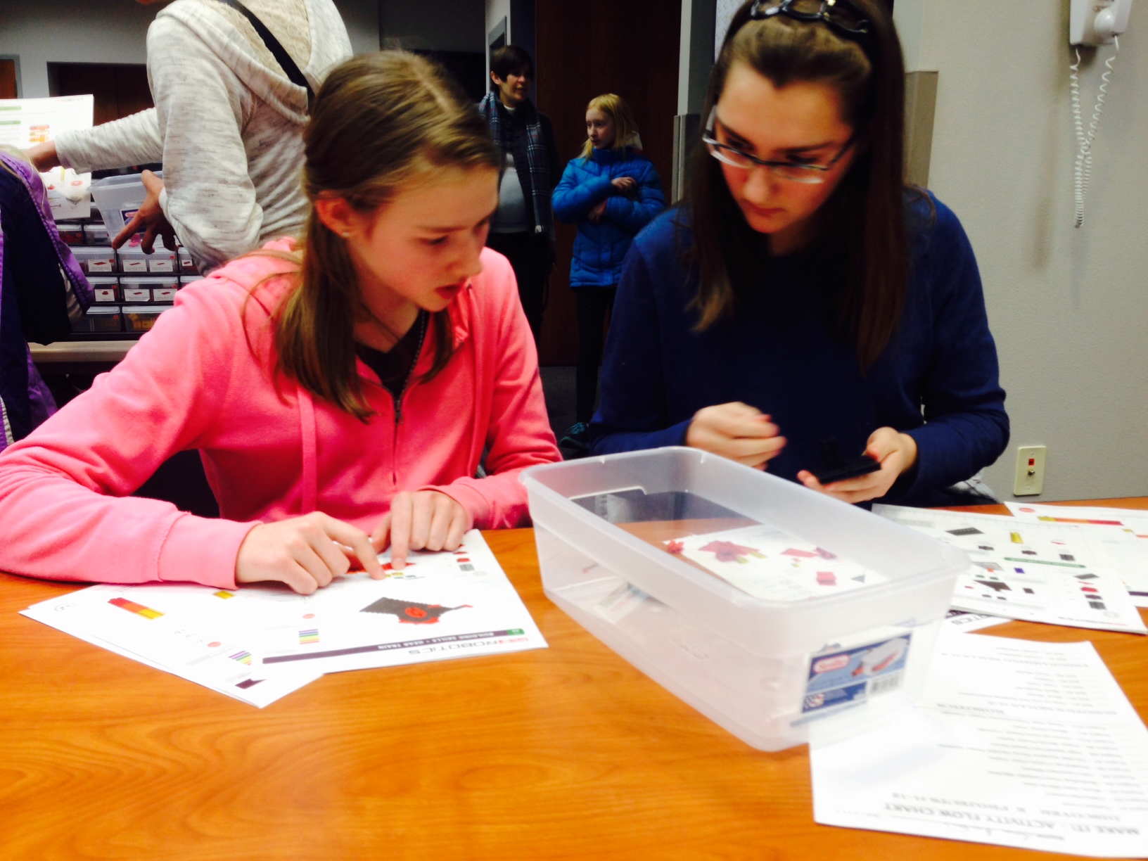 Two children reading instructions and building robots.
