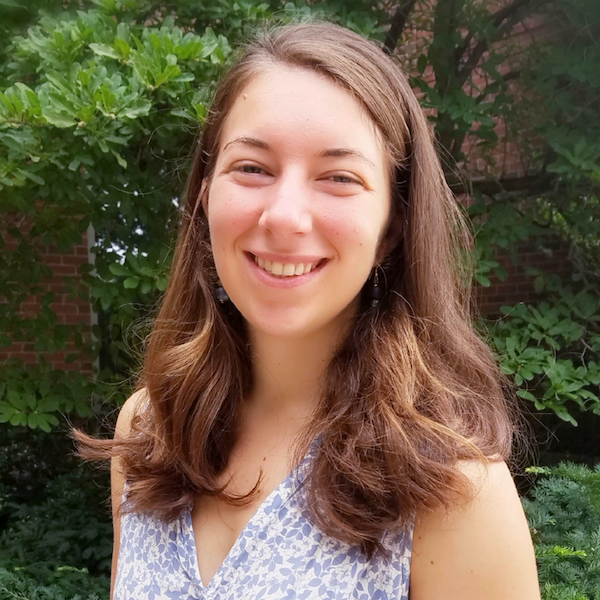 Kristiana, a young white woman with shoulder-length light brown hair, smiles at the camera while standing in front of a tree.