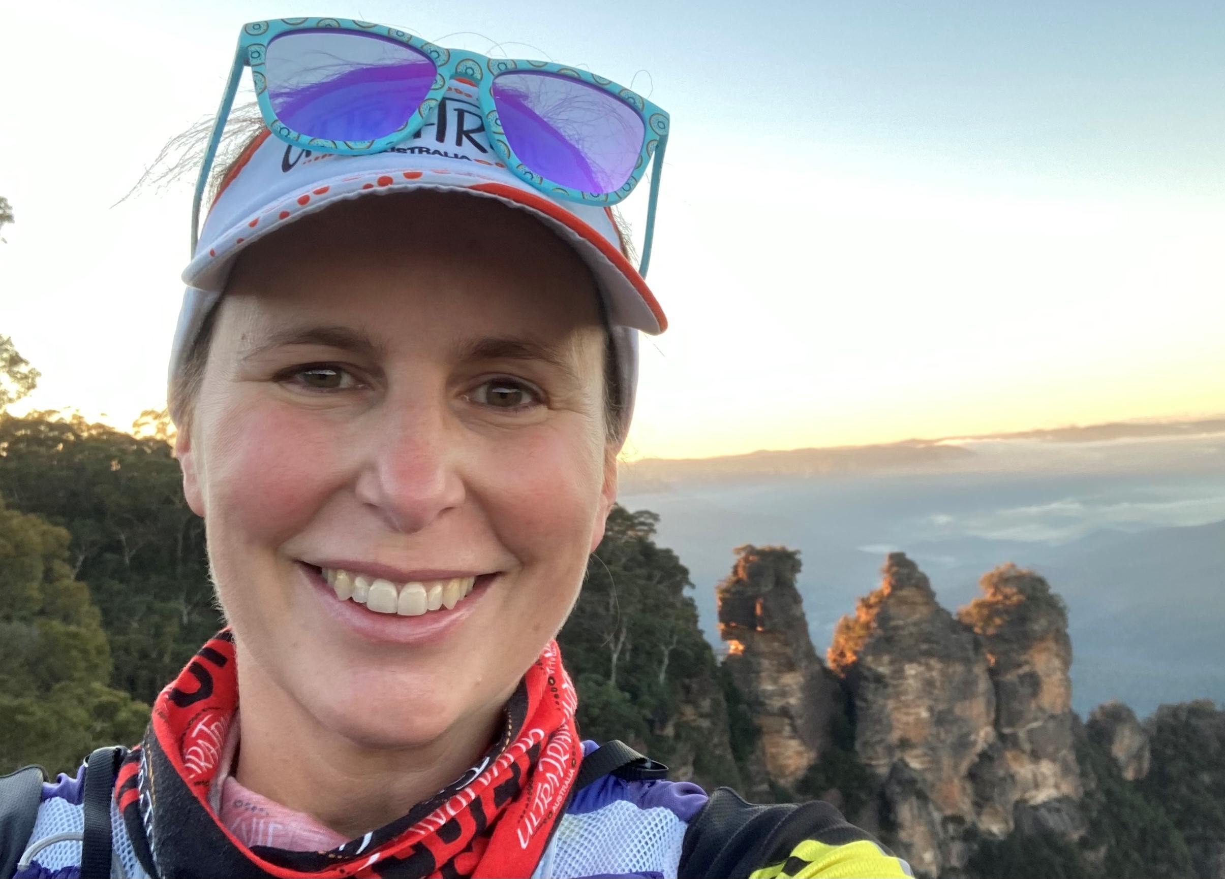 Serena in running gear smiling with dawn breaking over the 3 Sisters behind her