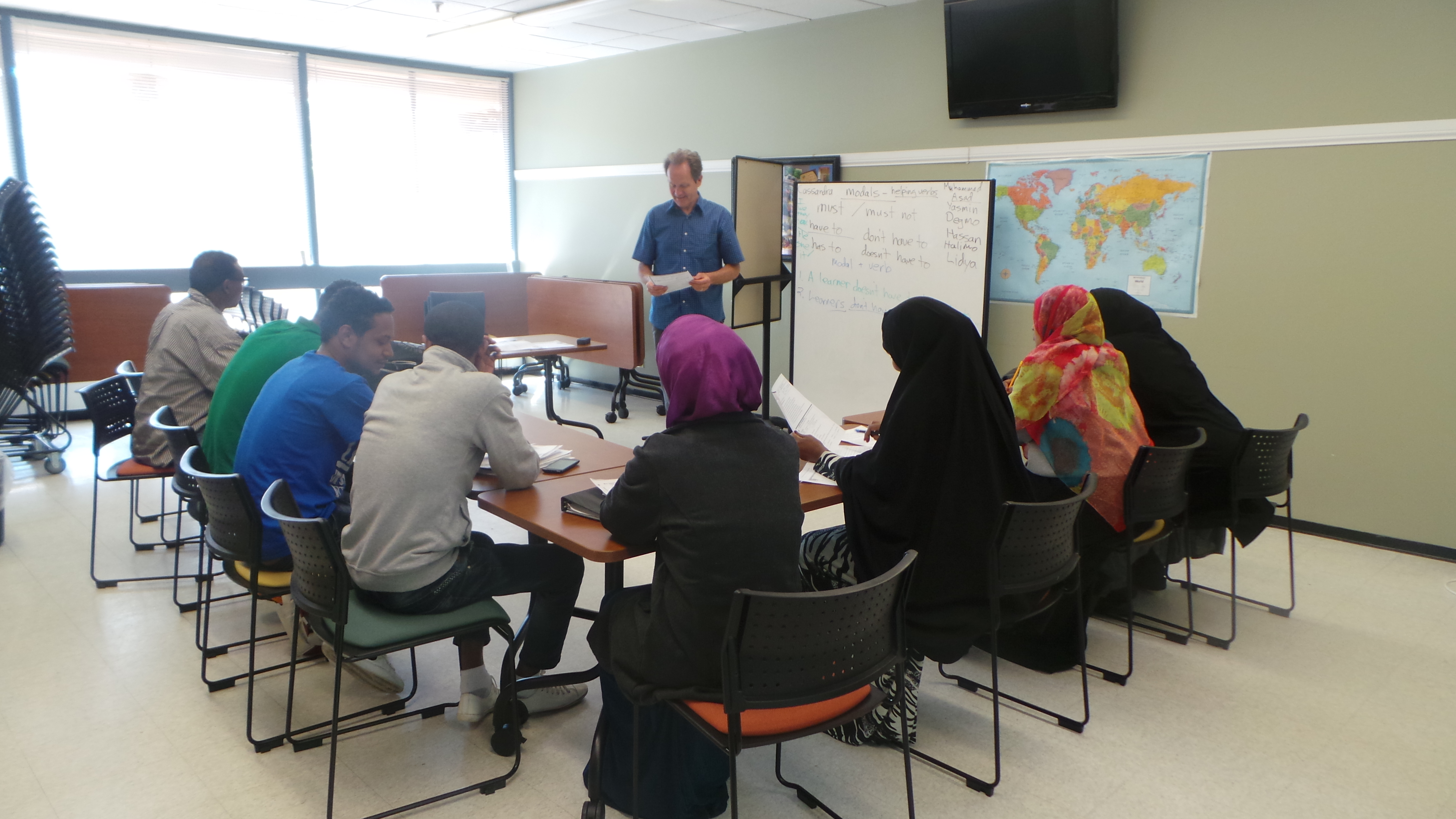 A classroom with a teacher in front and students seated at tables