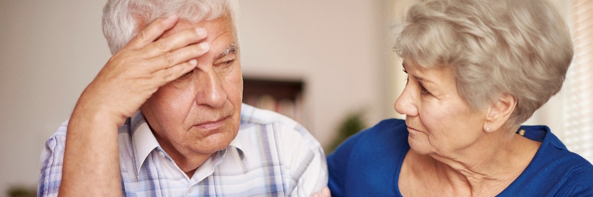 An older man with his hand on his head, being conforted by an older woman.