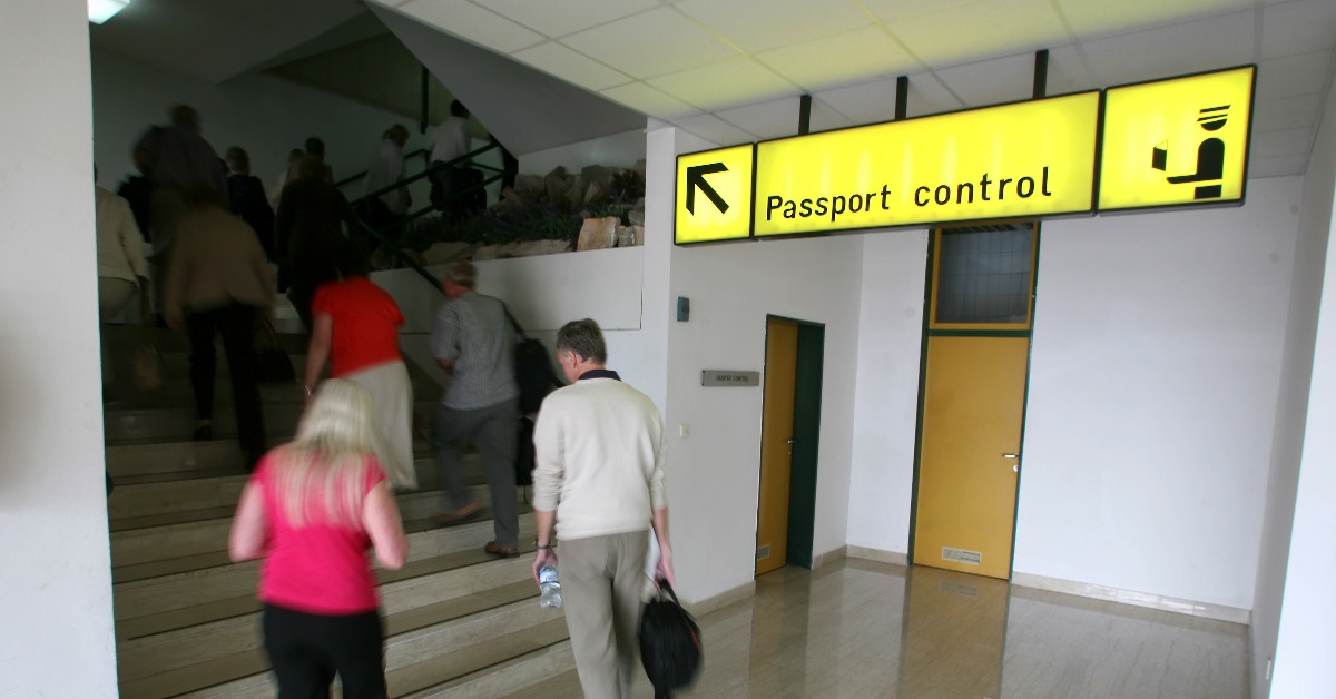 A sign pointing to passport control, with people climbing a flight of stairs in the background.