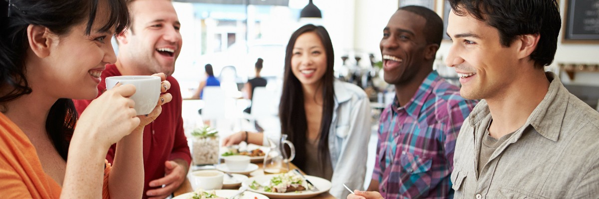 Five young people chatting over coffee and eating salads, possibly including avocado.