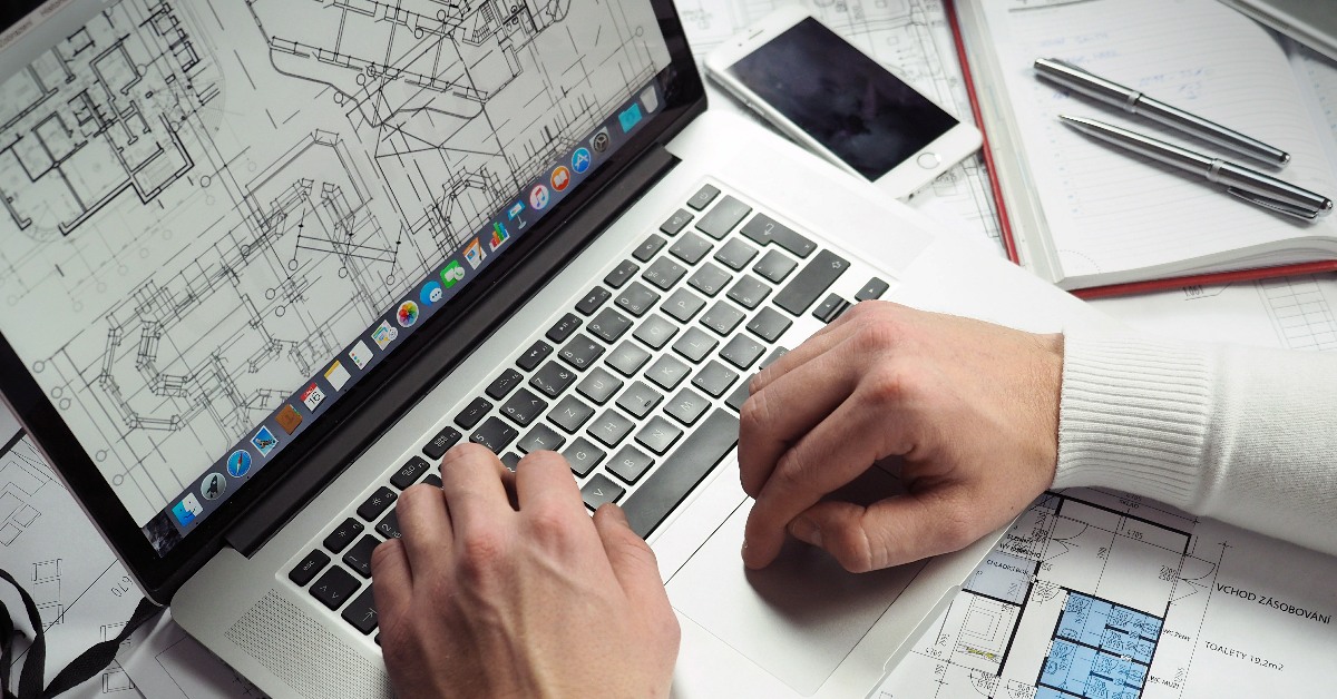 Plans on Macbook screen, hands operating laptop.