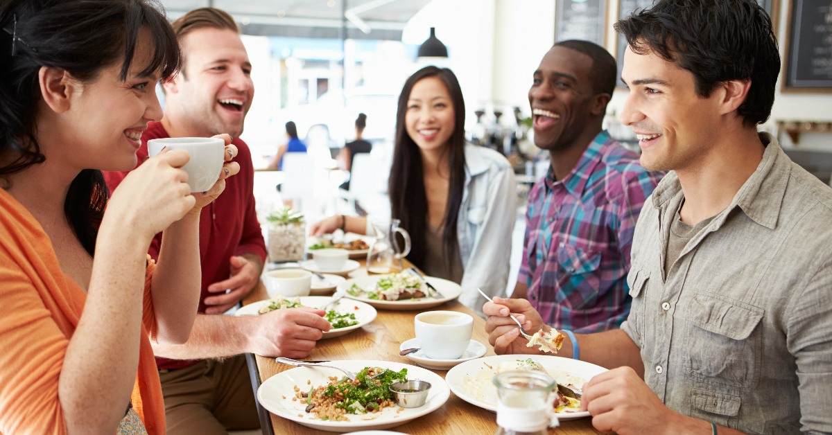 Five young people chatting over coffee and eating salads, possibly including avocado.