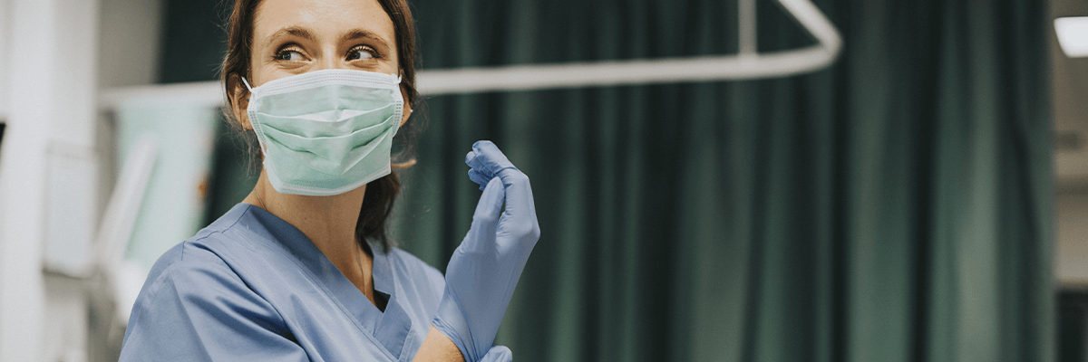 Medic in scrubs and mask pulling on a glove