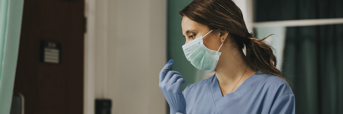 Medic in scrubs and mask pulling on a glove
