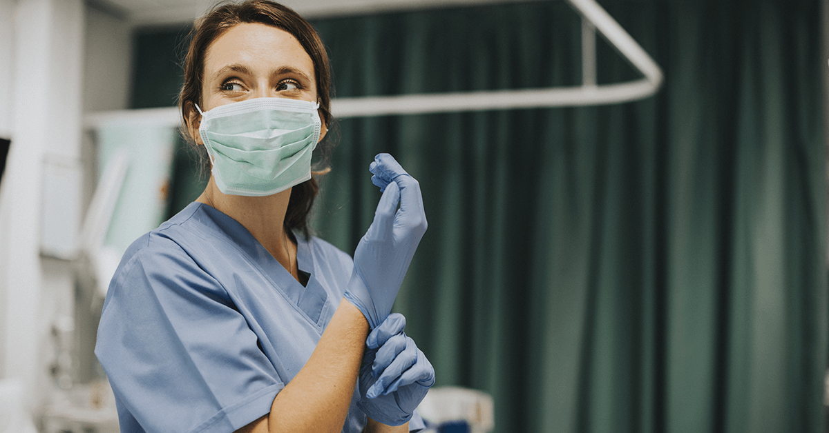 Medic in scrubs and mask pulling on a glove