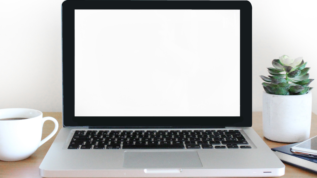 An open laptop on a desk with a coffee cup next to it.